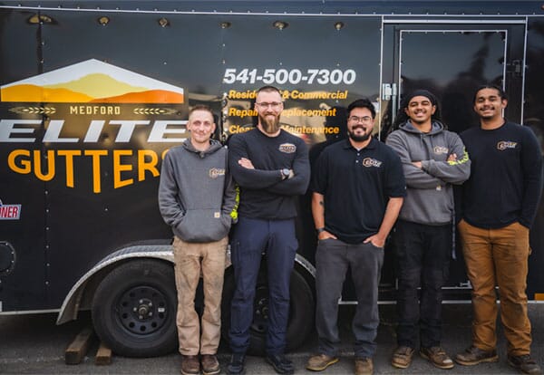 The Medford Elite Gutters team leans against their company trailer, smiling.